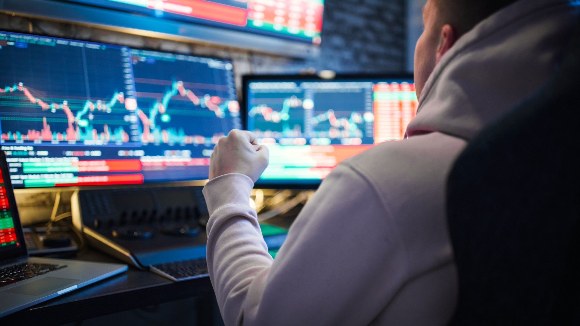 Young man with fist analysis at stock market graphs on computer screens at desk